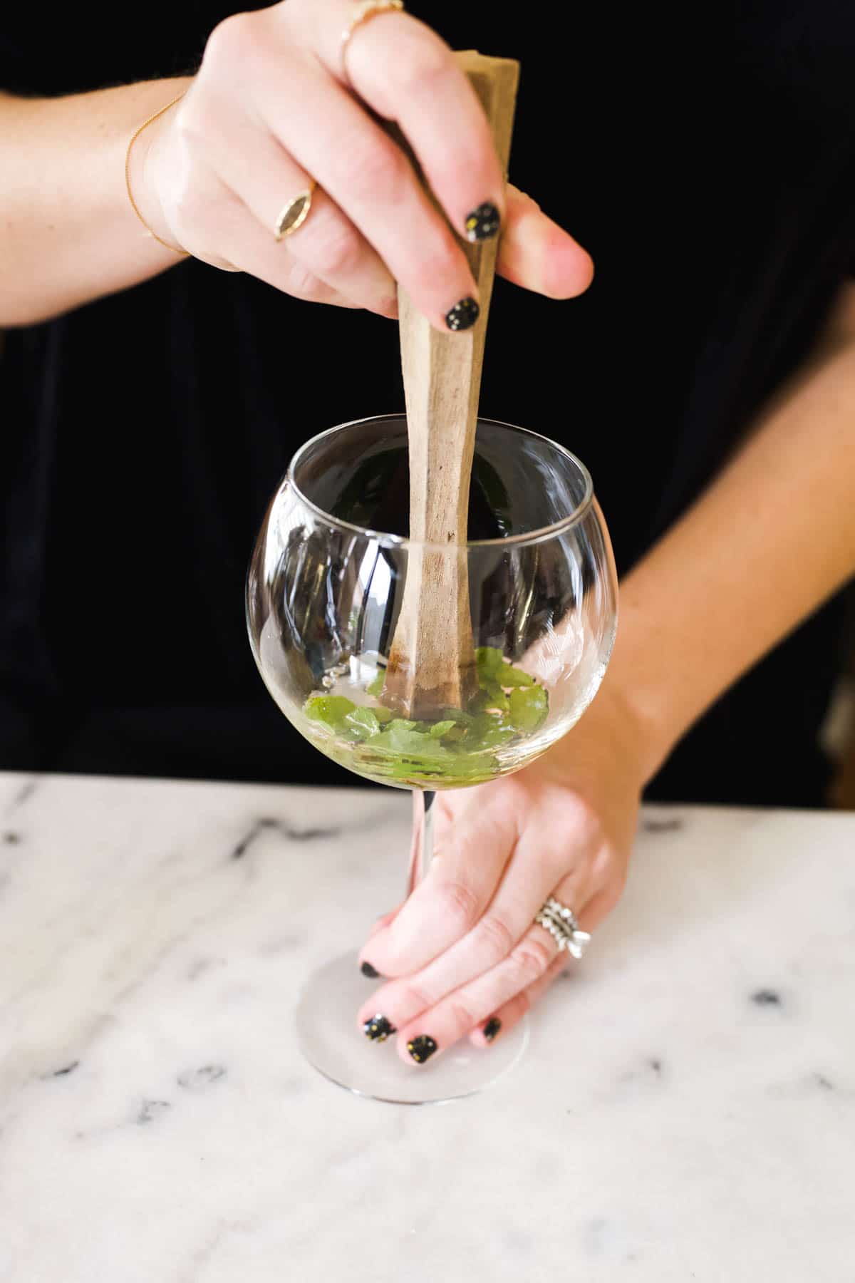 Mint being muddled in a balloon glass.