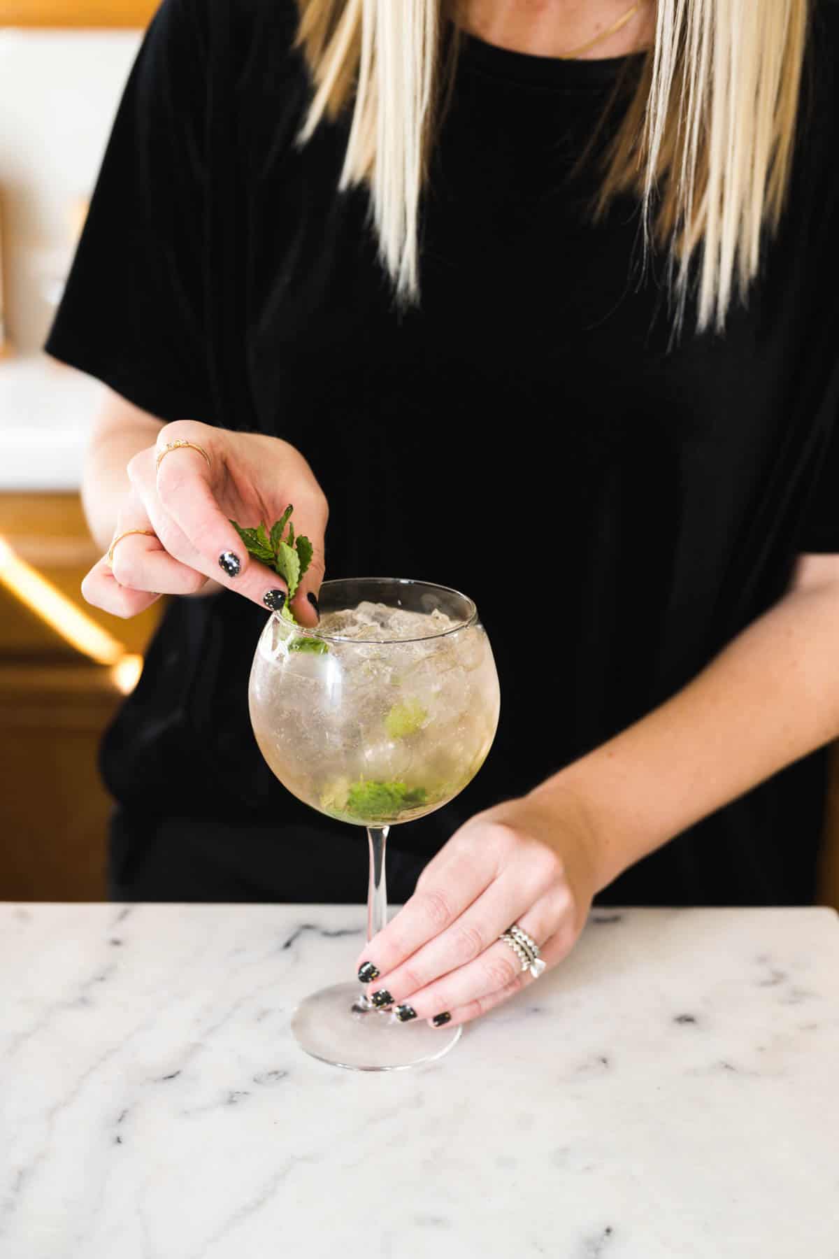 Woman garnishing a Hugo Spritz with fresh mint.