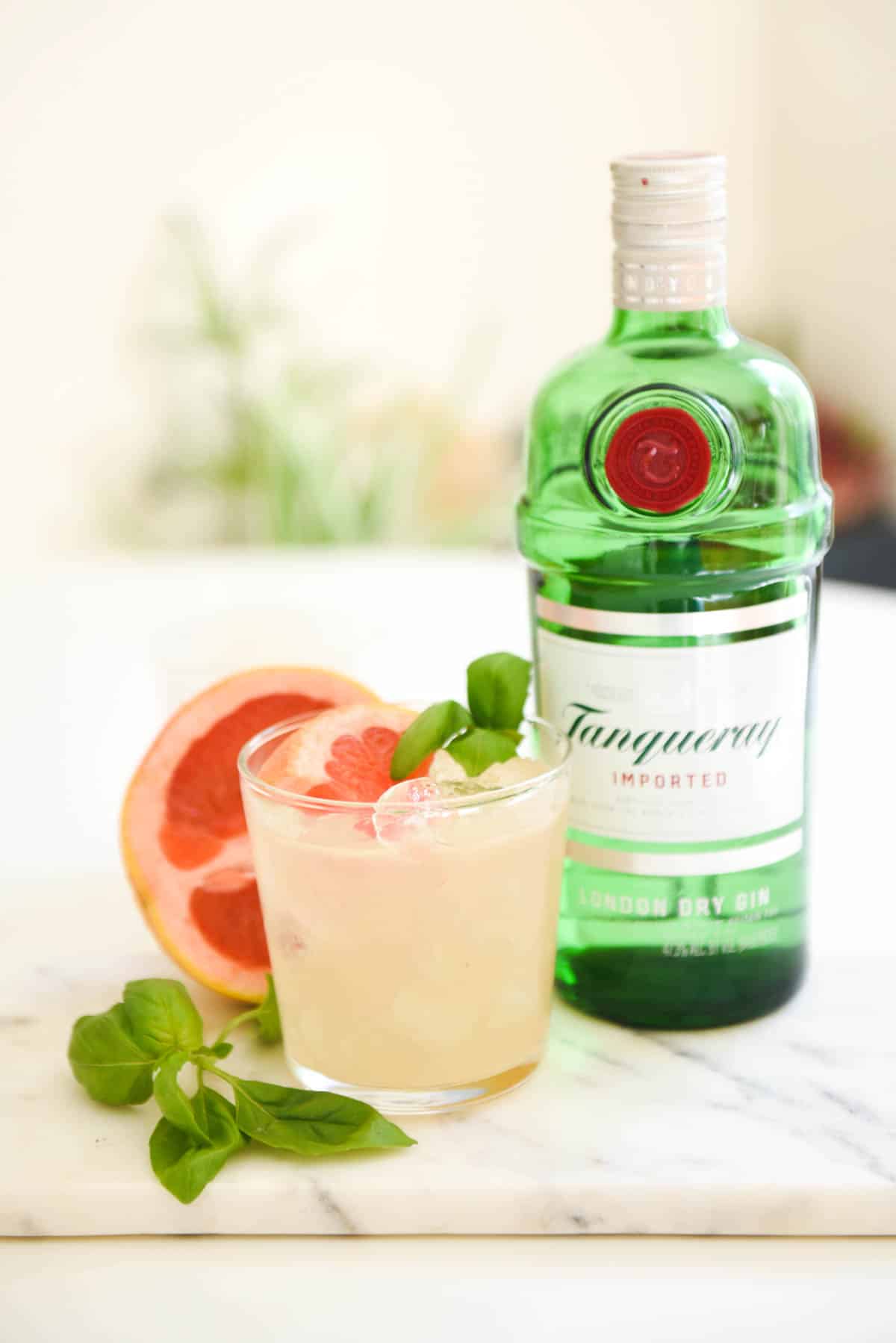 Grapefruit cocktail garnished with fresh basil next to a bottle of gin.