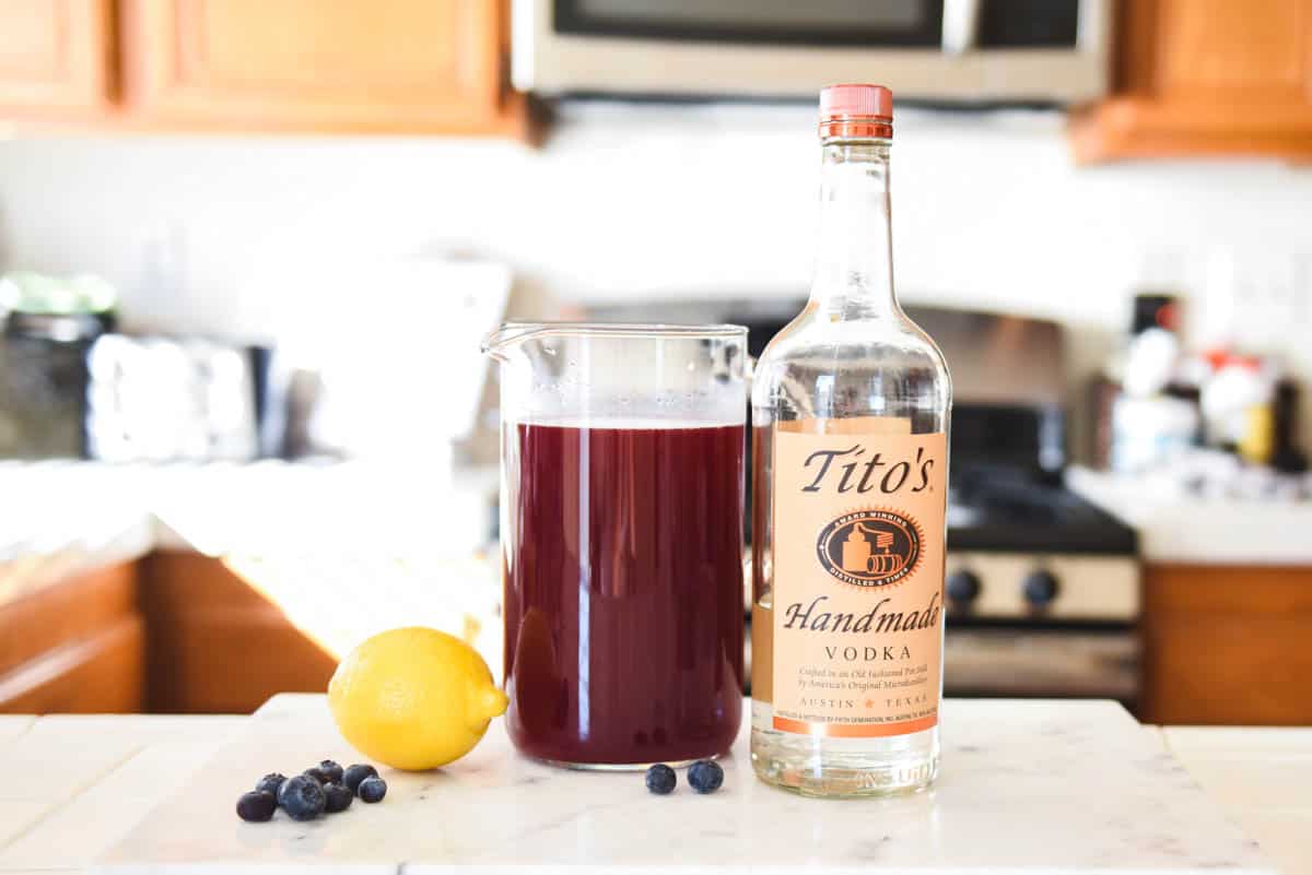 Ingredients to make a blueberry lemonade cocktail with vodka on a white kitchen counter.