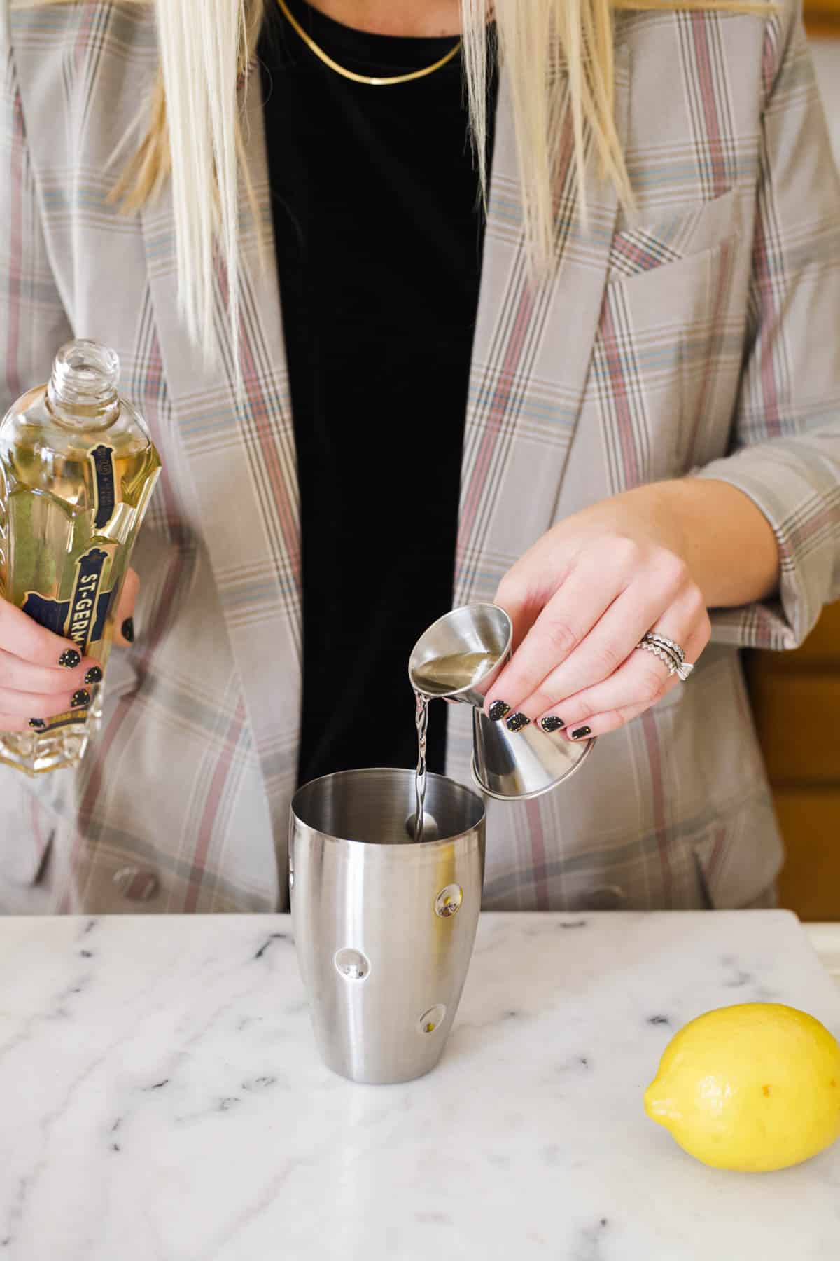 Woman pouring St Germain into a cocktail shaker.