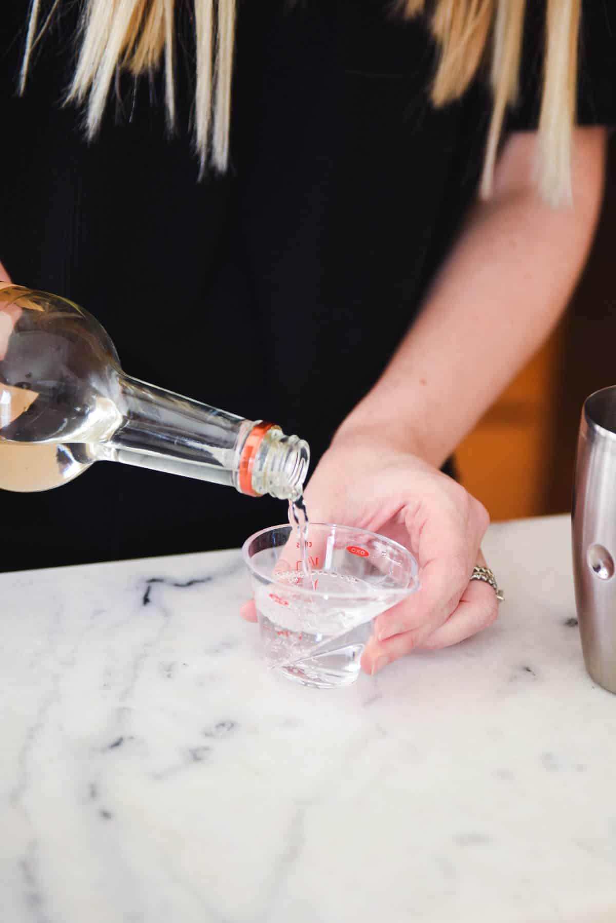 Woman adding vodka to a small measuring cup.