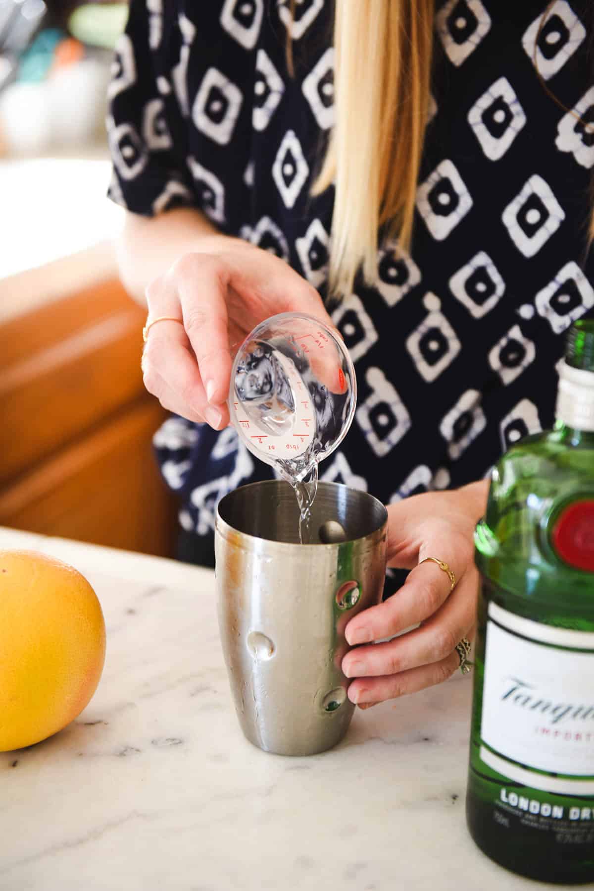 Woman pouring a measure of gin into a cocktail shaker.