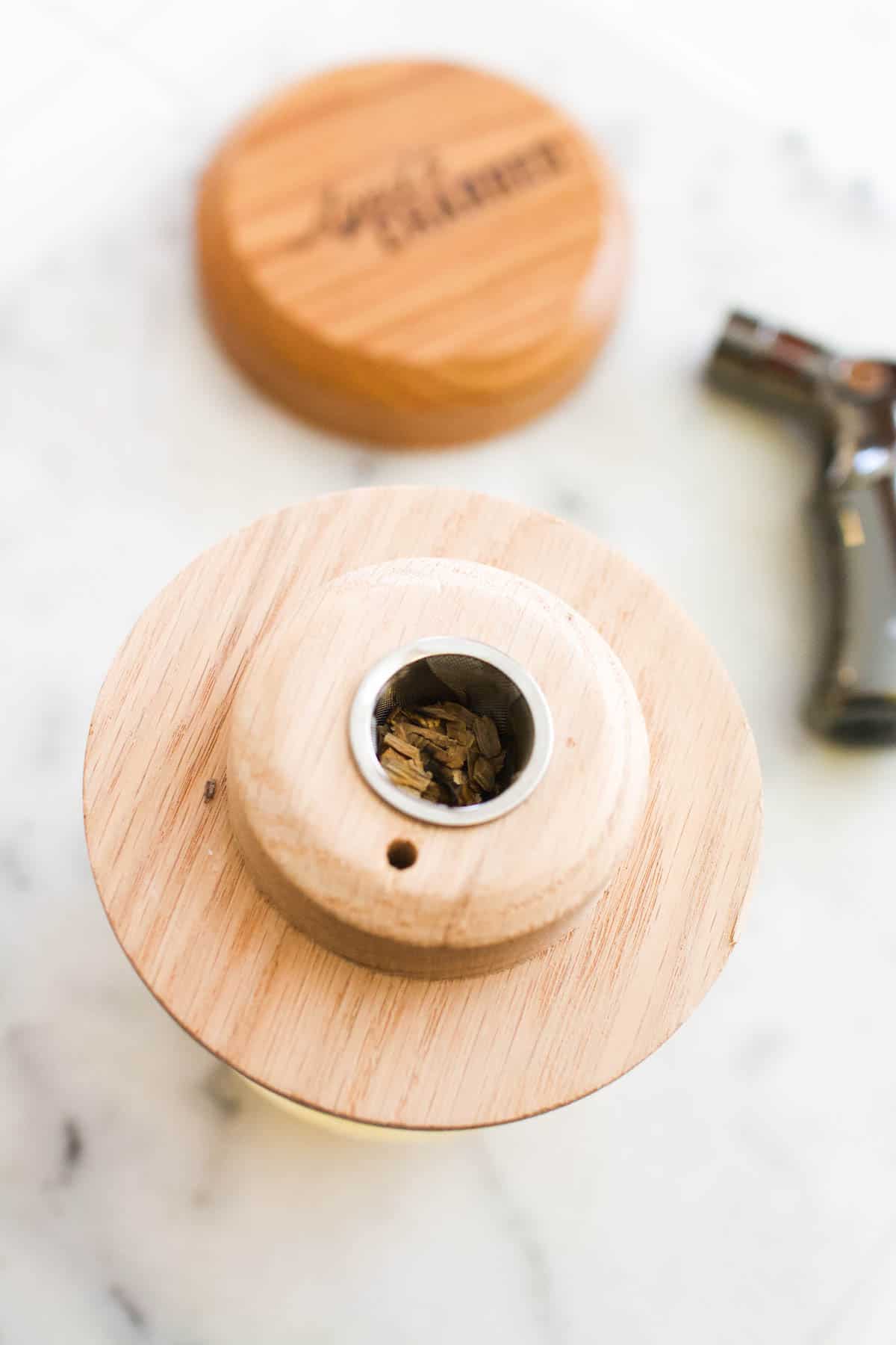 Wood chips in a cocktail smoker and lid, next to a butane torch.