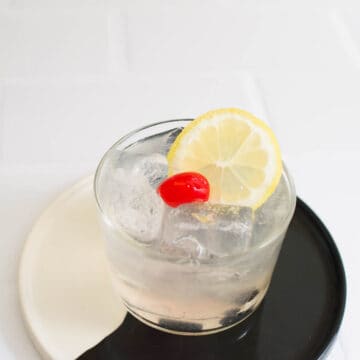 Vodka Sour garnished with a lemon wheel and cherry on a black and white tray.