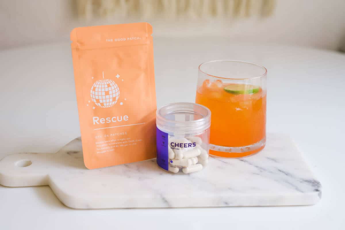 A collection of supplements to prevent hangover next to a cocktail on top of a marble cheese board.