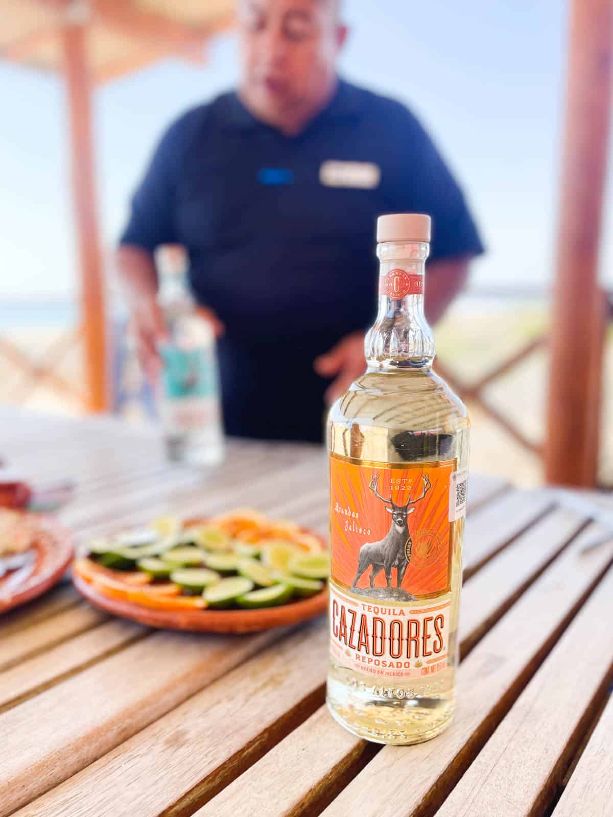 A bottle of Cazadores reposado tequila on a table next to a plate of sliced oranges and limes for a tequila tasting.