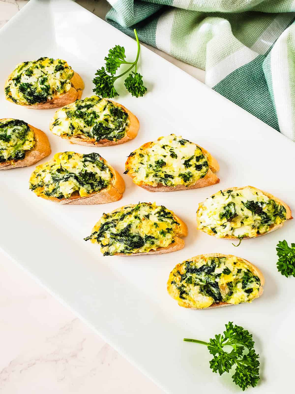 A platter with baked artichoke and spinach dip on sliced baguette.