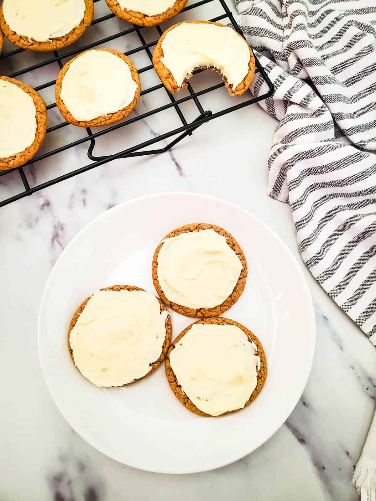 Frosted Carrot Cake Mix cookies on a wire rack and a white dessert plate.