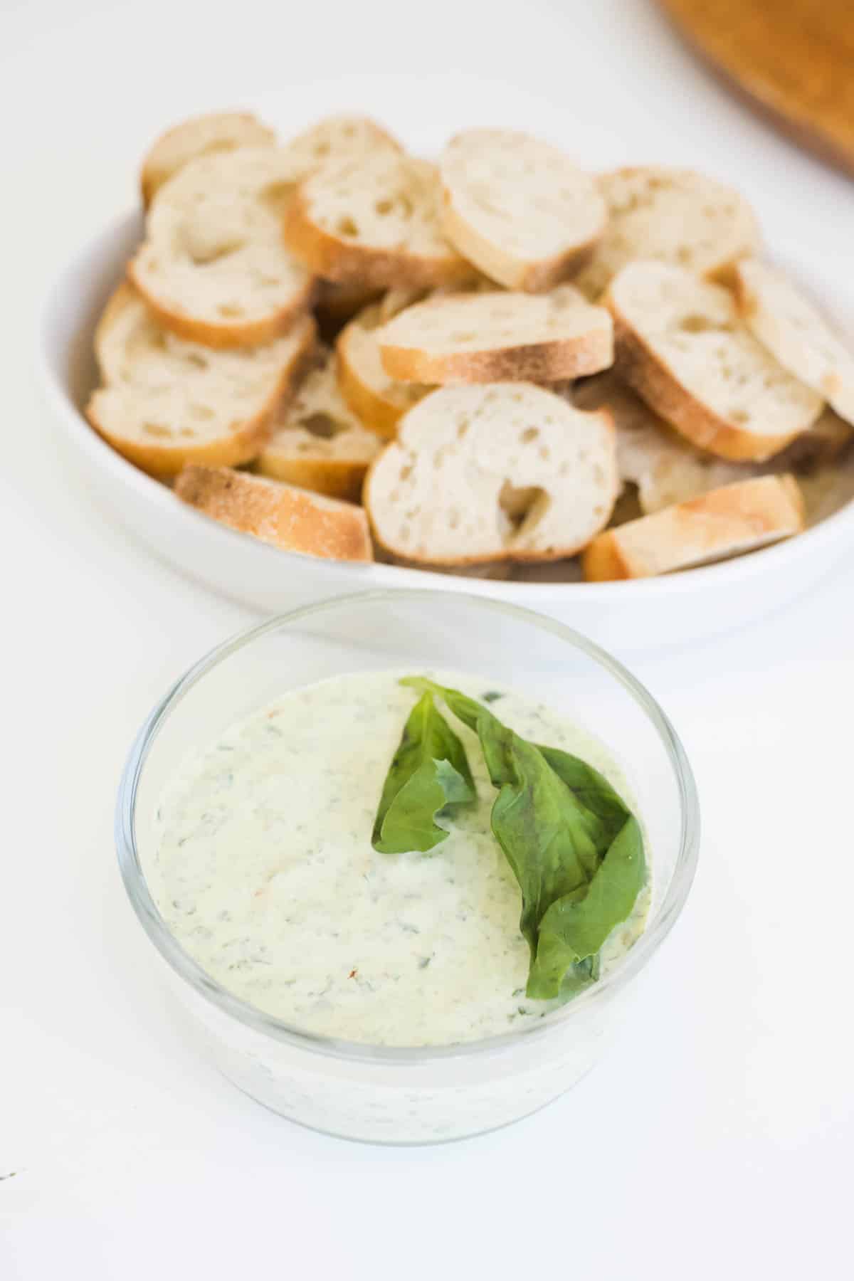 Two bowls, one filled with green goddess dip and one filled with crostini.