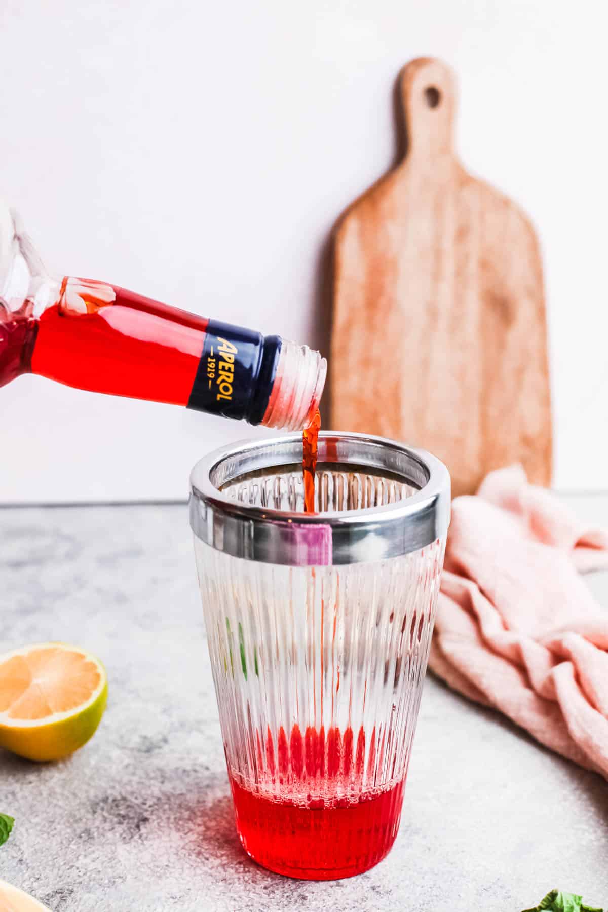 Woman adding Aperol to a cocktail shaker for a coconut daiquiri.