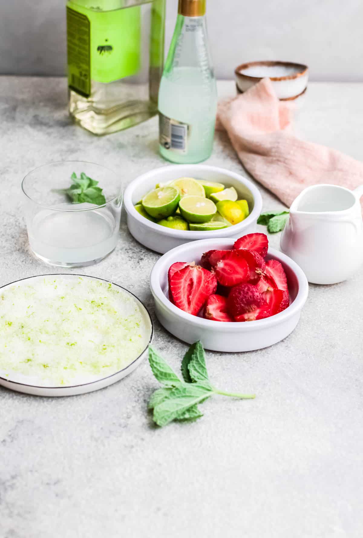 Ingredients to make a strawberry tequila cocktail in shallow white bowls.