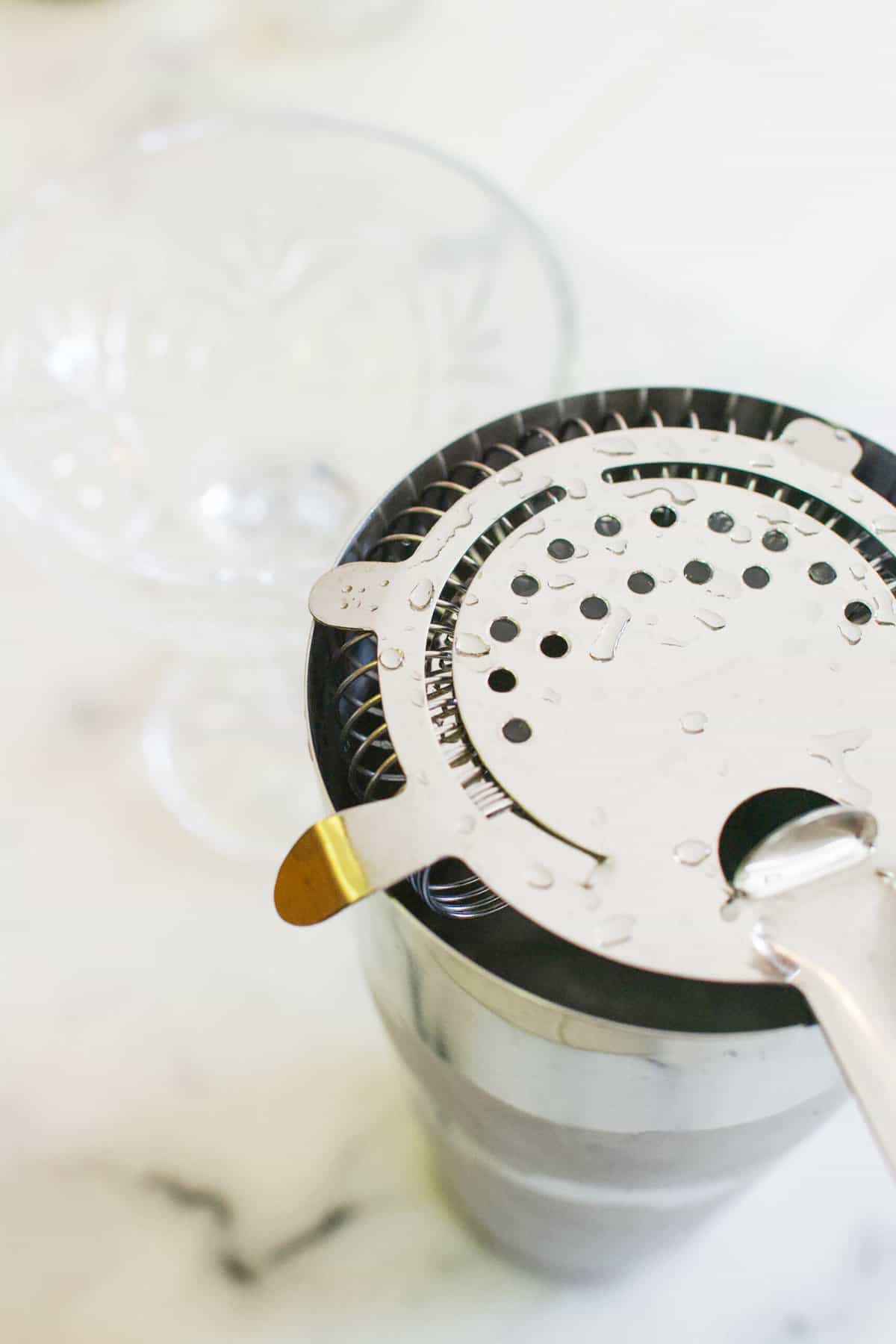 Cocktail shaker fitted with a strainer next to a coupe glass.