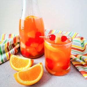 Close up of passion fruit sangria in a cup with the rest of the cocktail next to a pitcher.