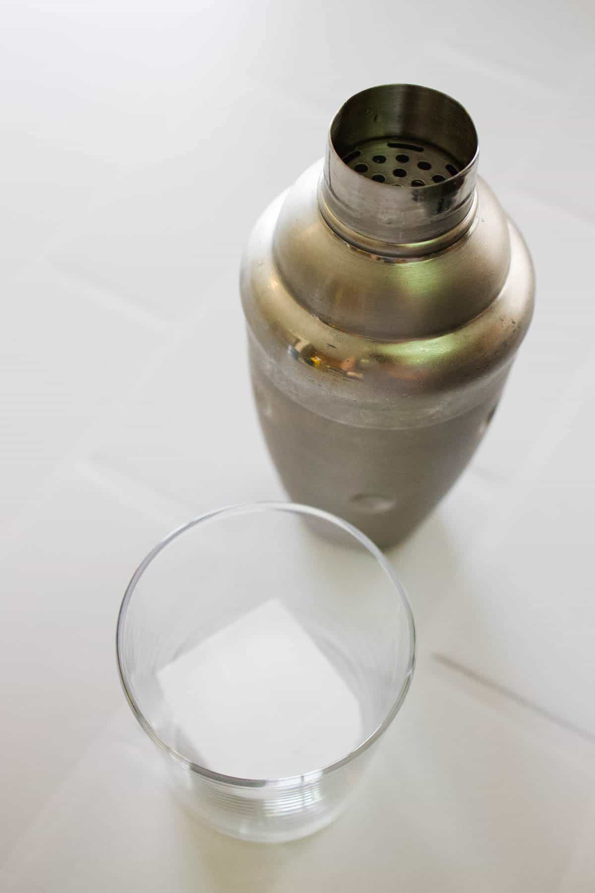 Cocktail shaker next to a glass with a giant ice cube.