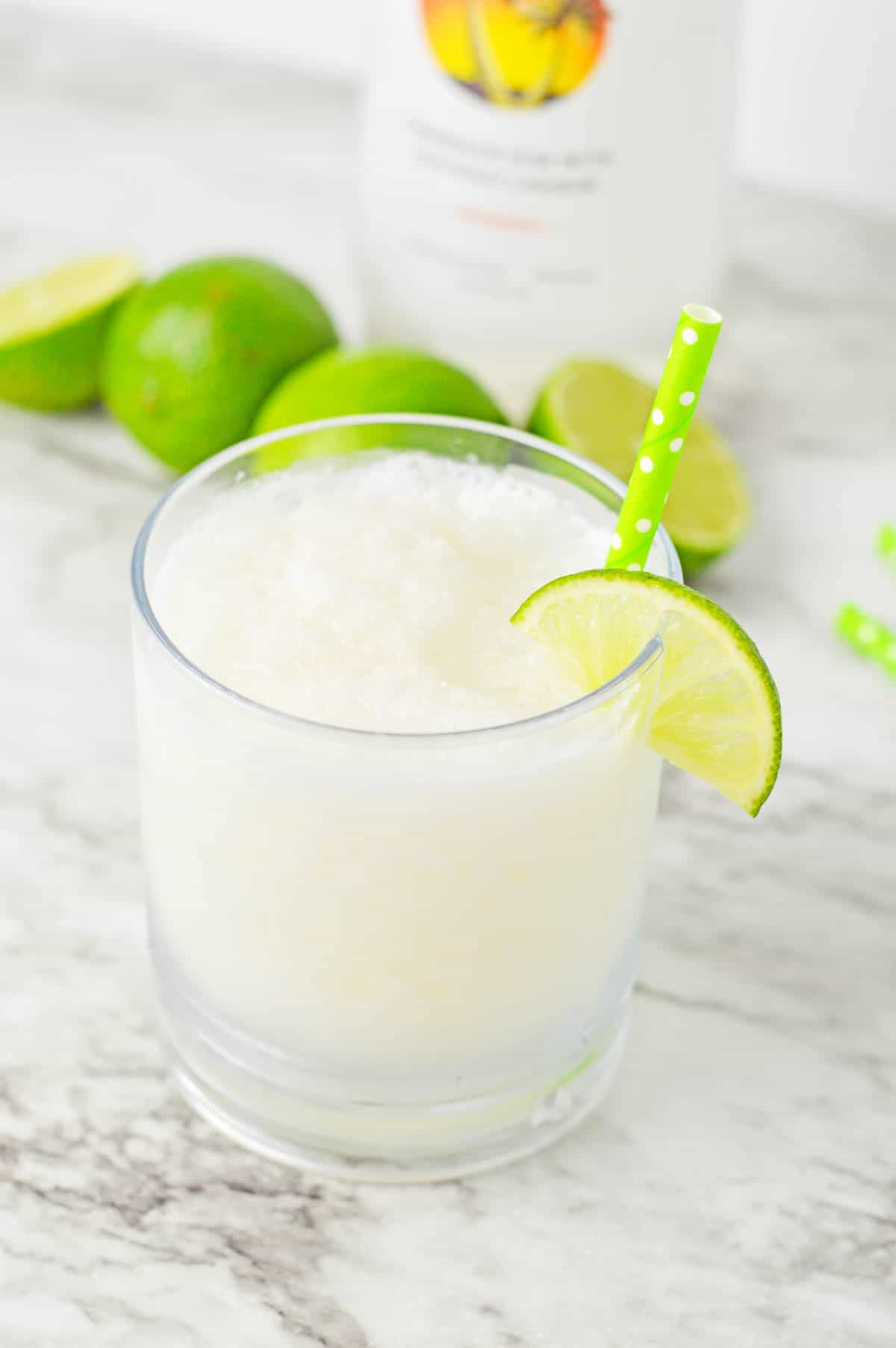 Frozen Malibu daiquiri in a short glass garnished with a lime wedge and a green paper straw.