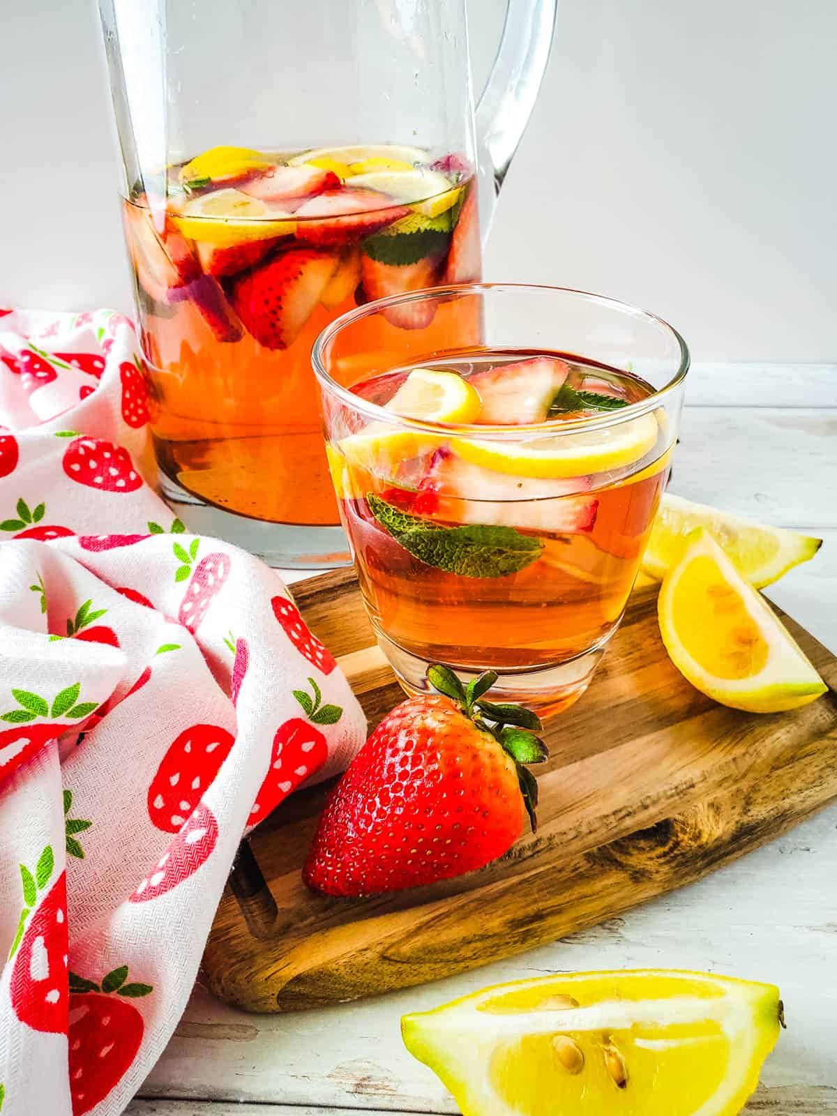 Class and pitcher of sangria on a wooden cutting board.