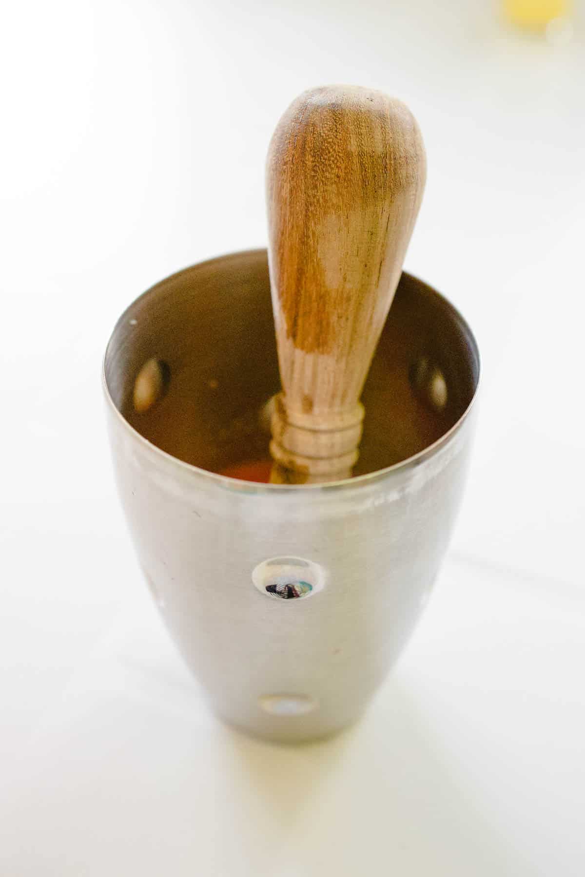 Wooden muddler sitting in a metal cocktail shaker.