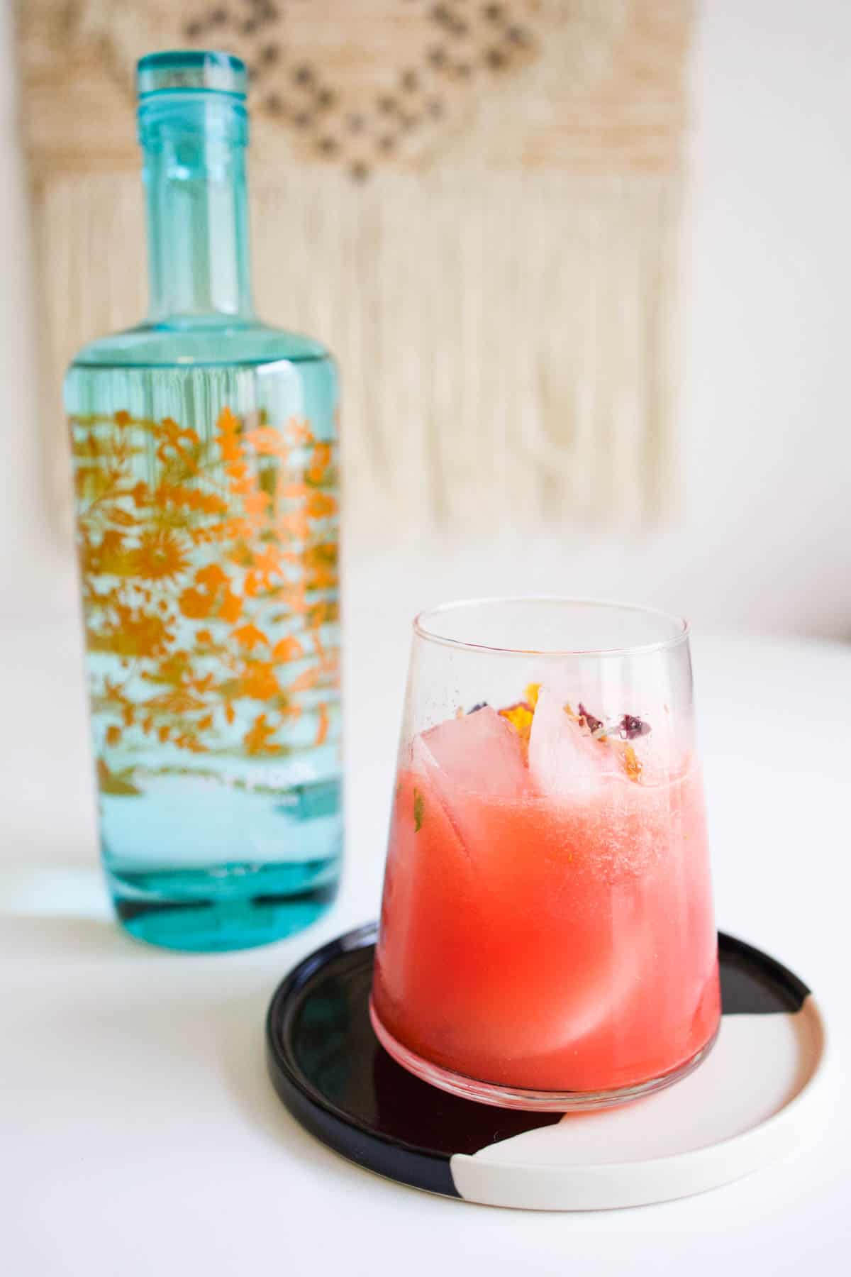 Gin and watermelon cocktail on a black and white serving platter with a blue bottle of gin in the background.