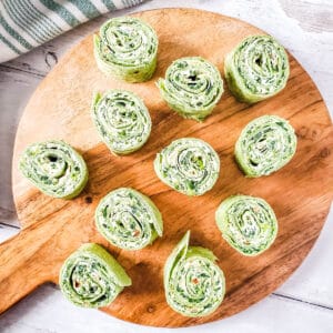 Spinach artichoke dip pinwheels on a wood platter.