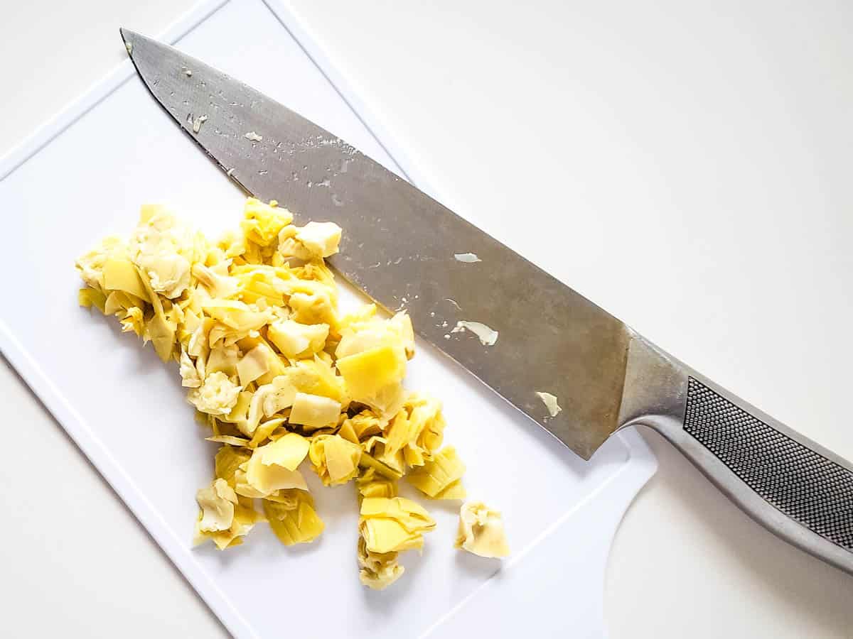 A small white cutting board topped with chopped artichokes next to a chef's knife.