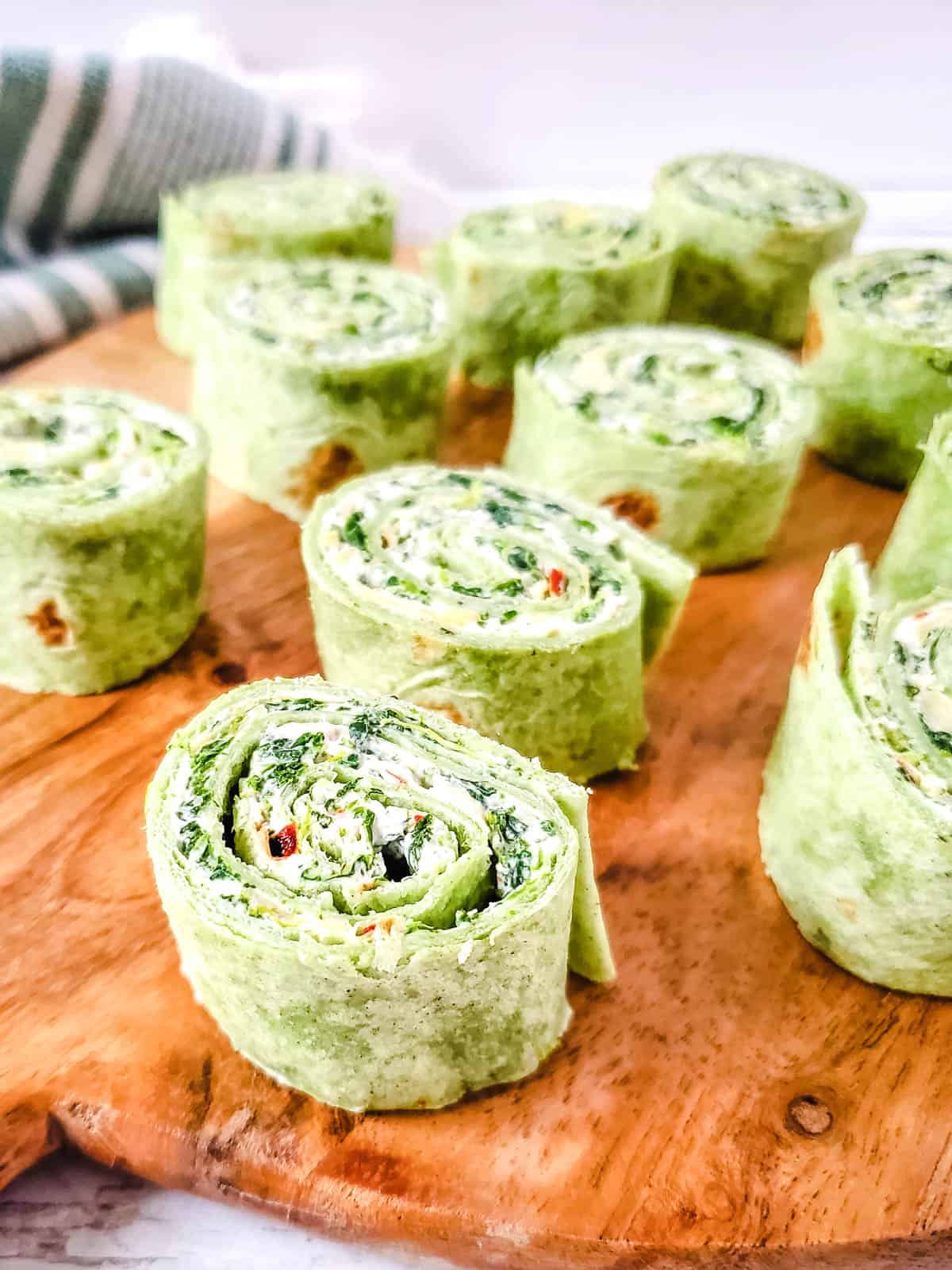 Spinach artichoke pinwheels on a wooden platter.