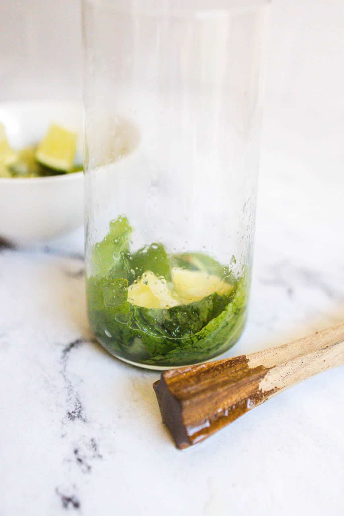 Muddled mint and lime in the bottom of a glass,