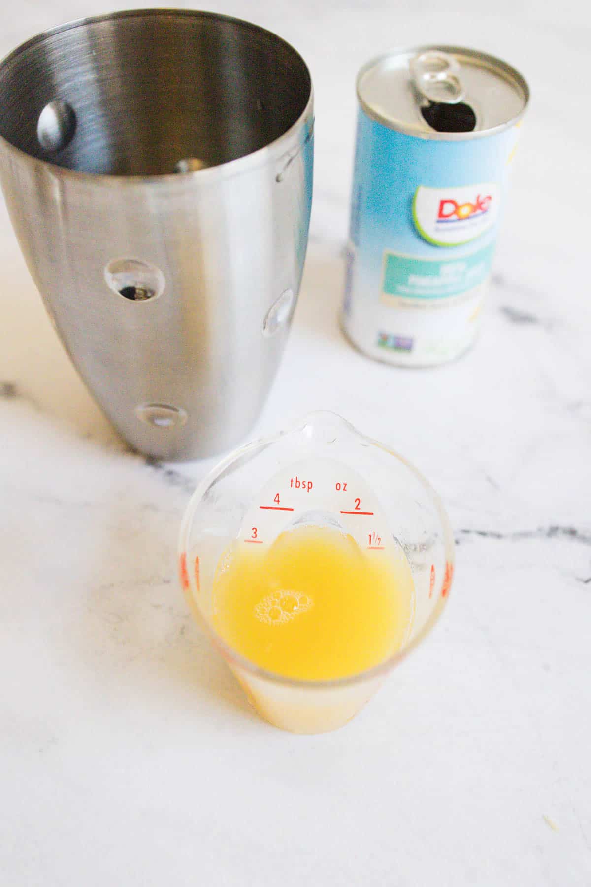 Pineapple juice being measured into a cocktail shaker.