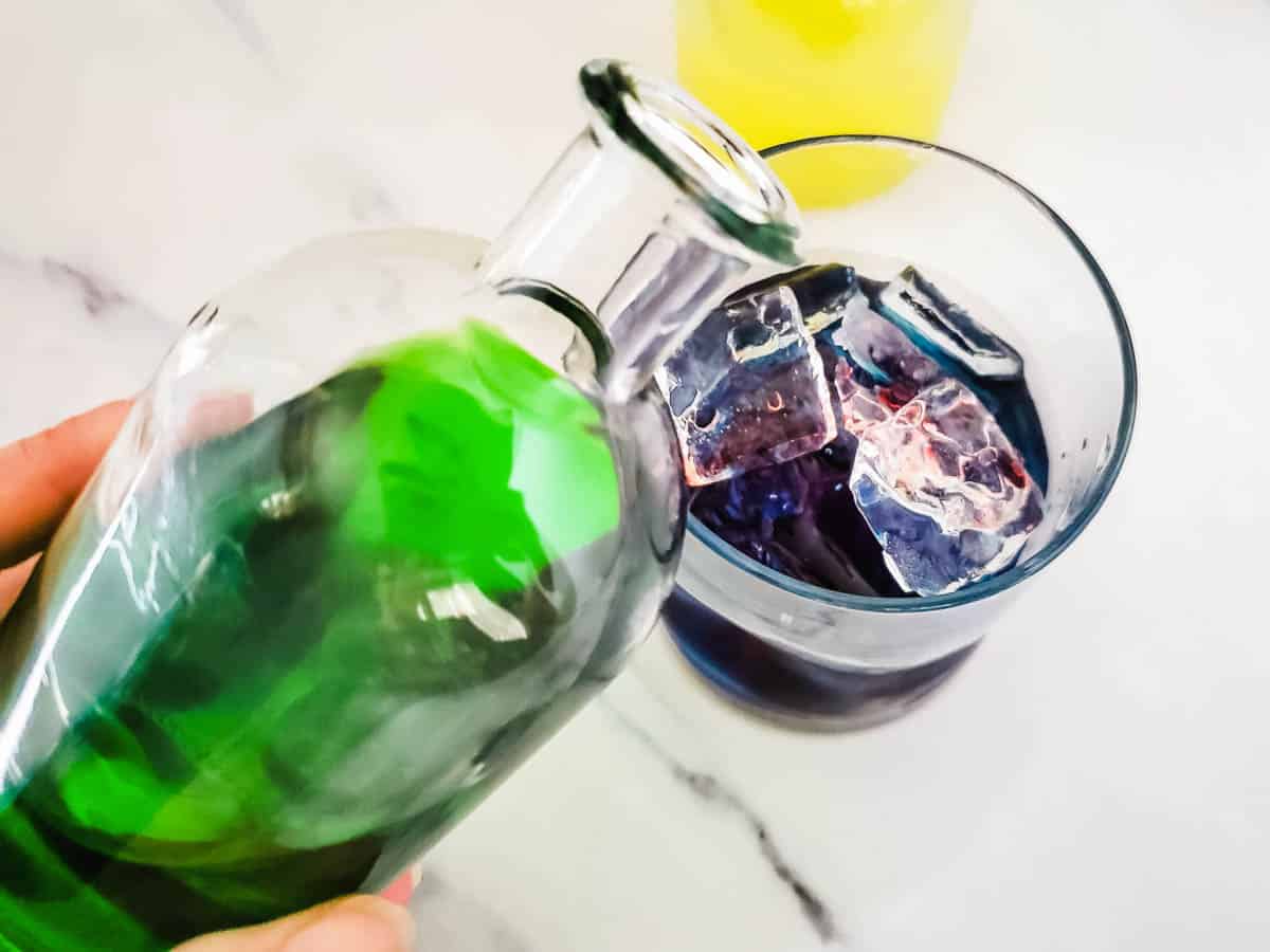 Green apple syrup being poured over a Halloween cocktail n a glass of ice.