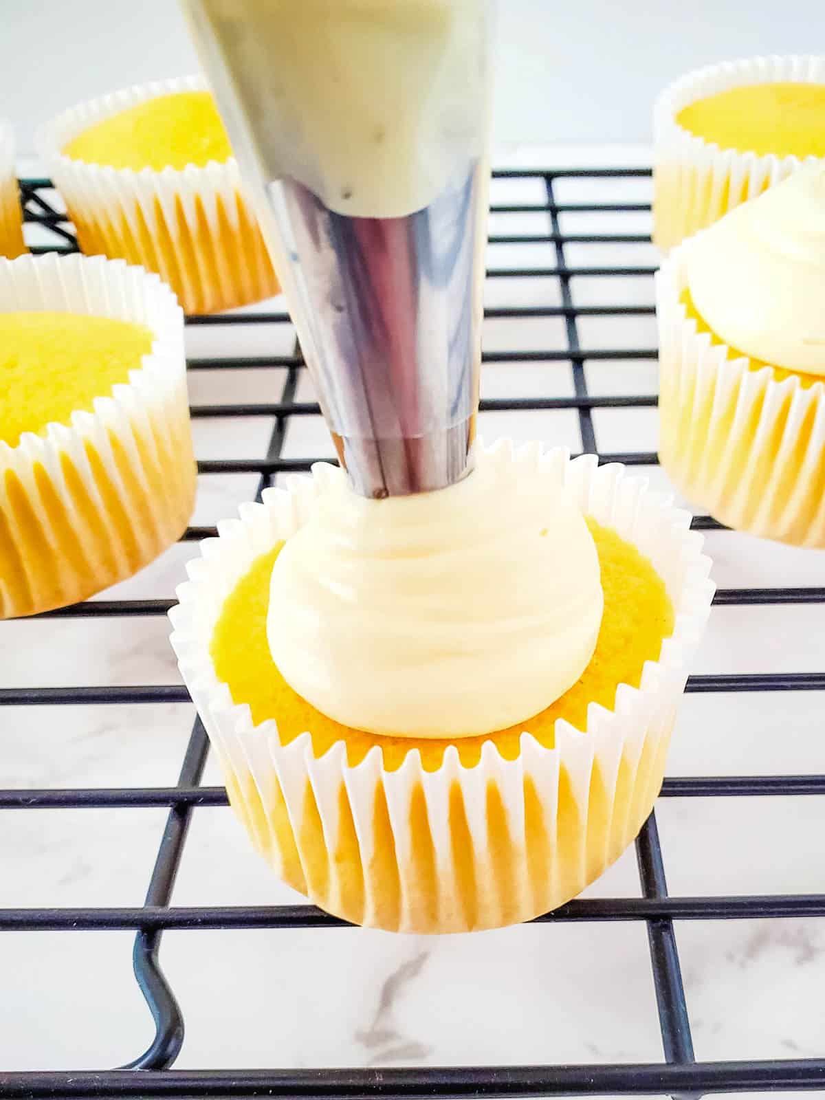 Piping buttercream frosting on spiced rum cupcakes on a wire rack.