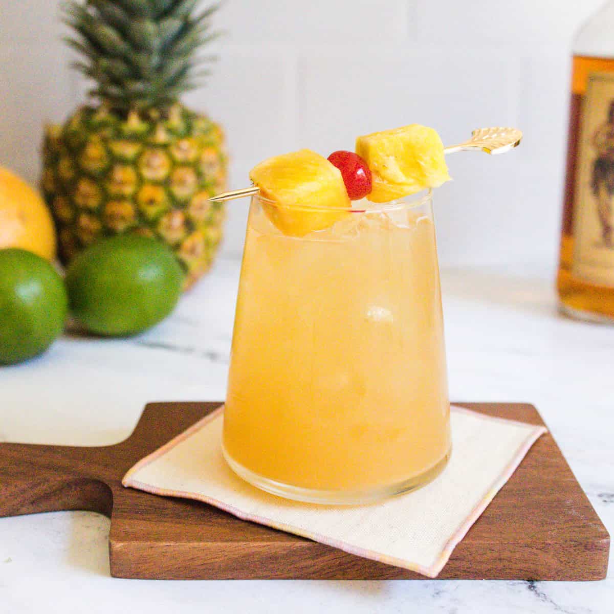 Tropical rum cocktail garnished with a cocktail tick of pineapple chunks and a cocktail cherry.