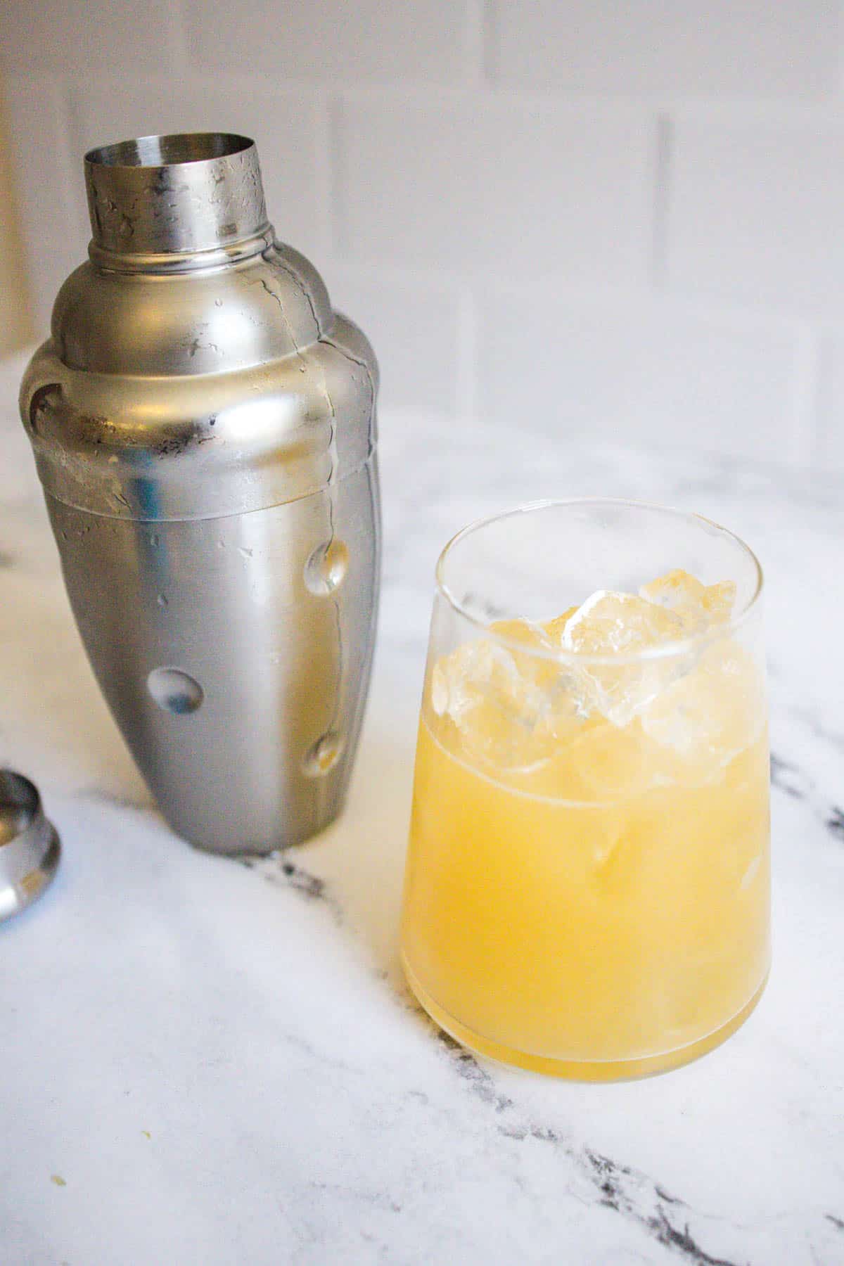 Pineapple juice cocktail over ice next to a chilled cocktail shaker.