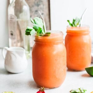 Two frozen cocktails in ball jars garnished with fresh mint sprigs and metal straws.