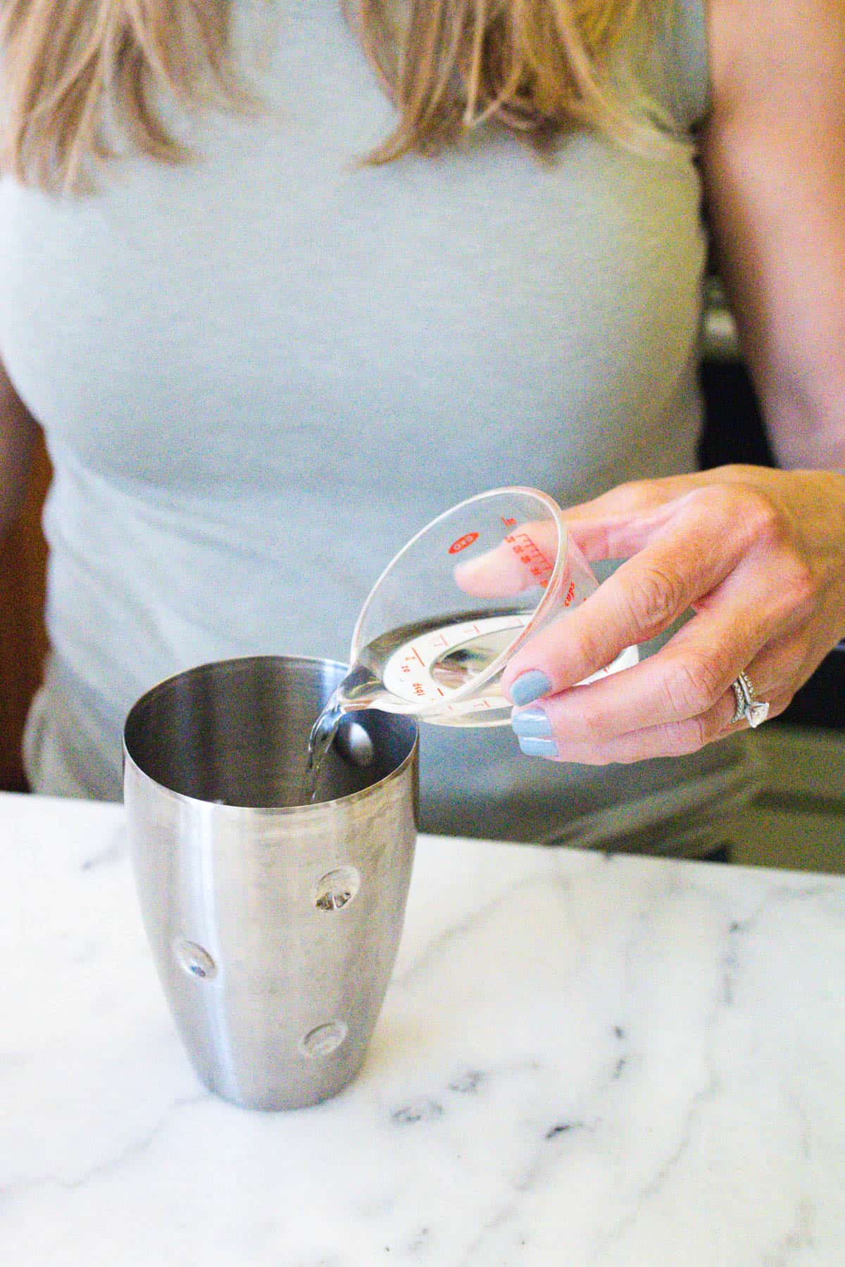 Woman measuring tequila into a cocktail shaker. 