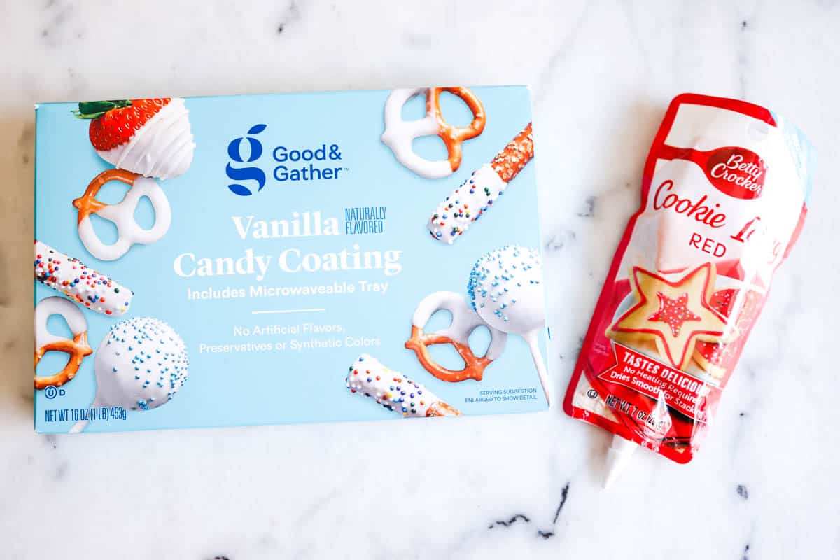 A box of white chocolate for melting next to a red icing tube on a table.