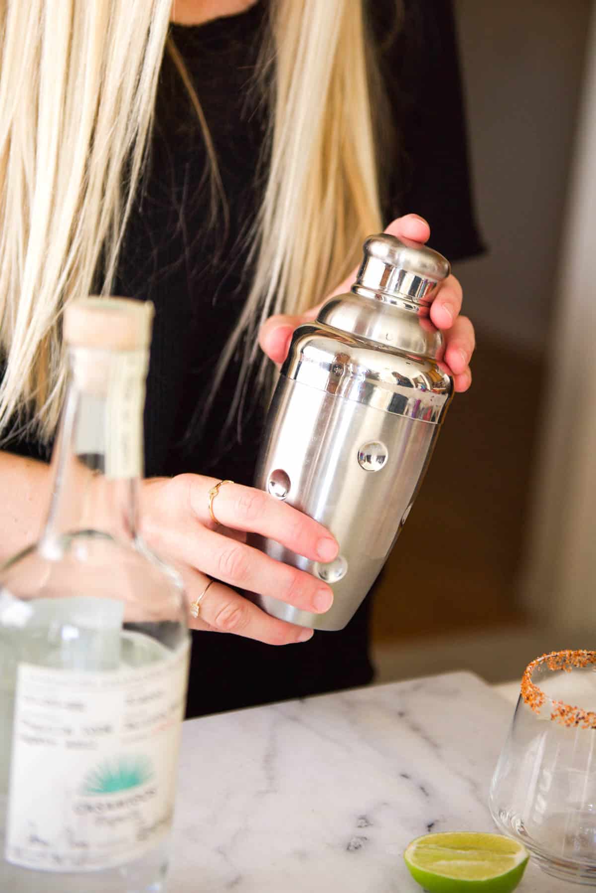 Woman shaking a silver cocktail shaker.