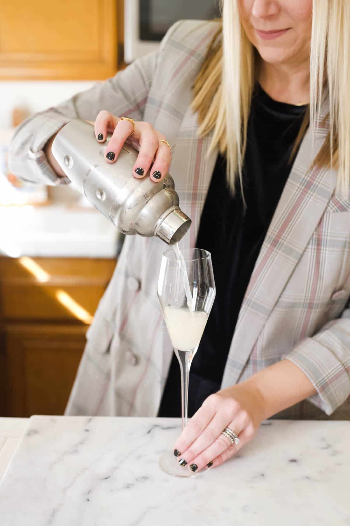 Woman straining a drink into a champagne glass.