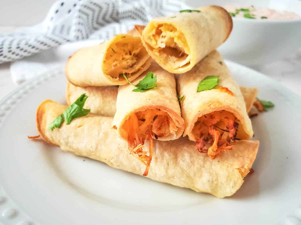 Close up view of air fryer corn tortilla chicken taquitos piled on a plate. 