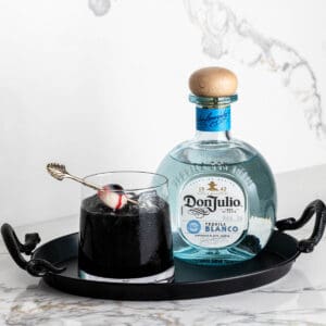 A black drink for Halloween on a tray next to a bottle of Don Julio tequila.