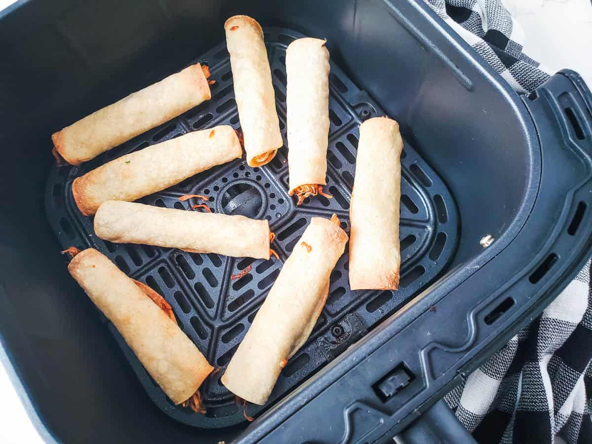 Cooked chicken taquitos in an air fryer basket.