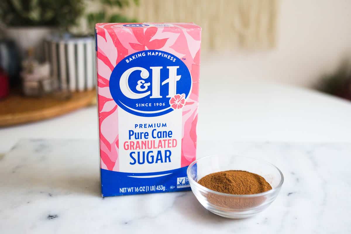 Box of granulated sugar on the countertop next to a small glass bowl of ground cinnamon.