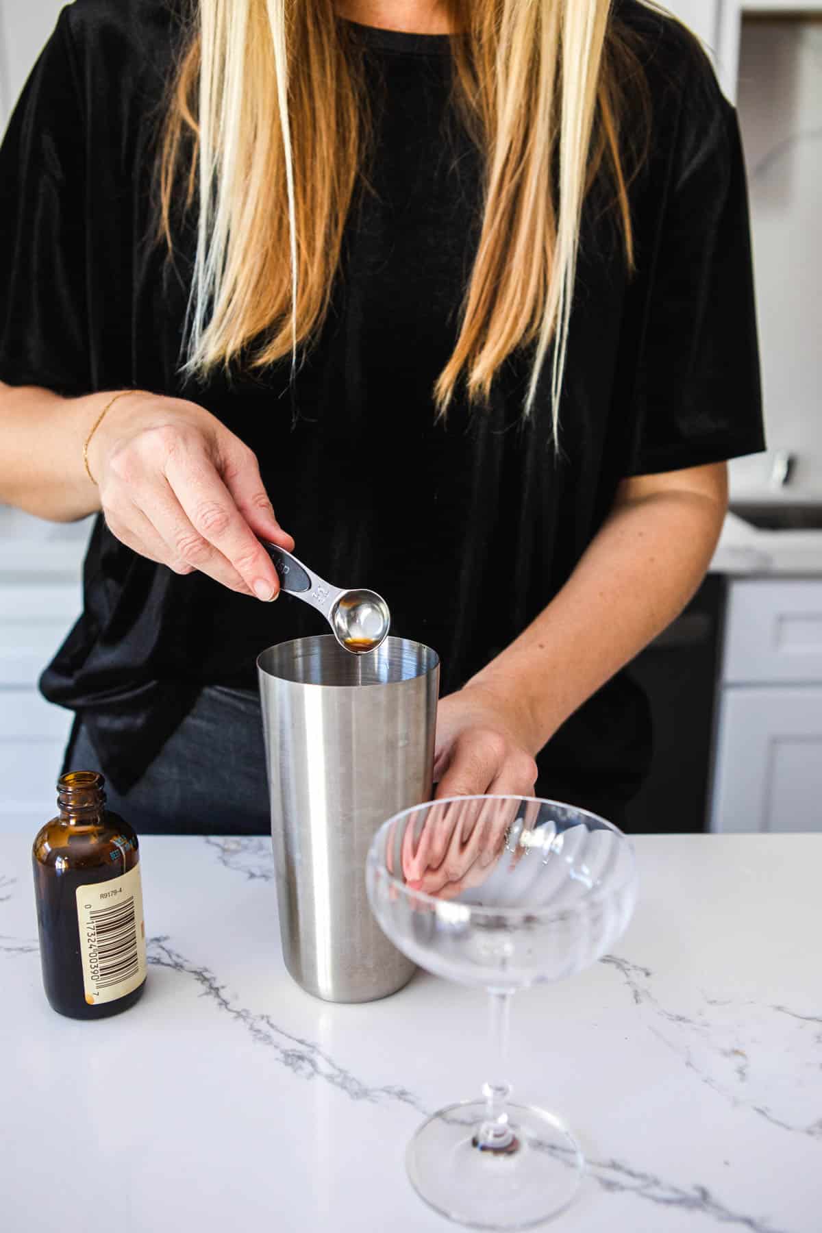 Woman measuring vanilla into a cocktail shaker.