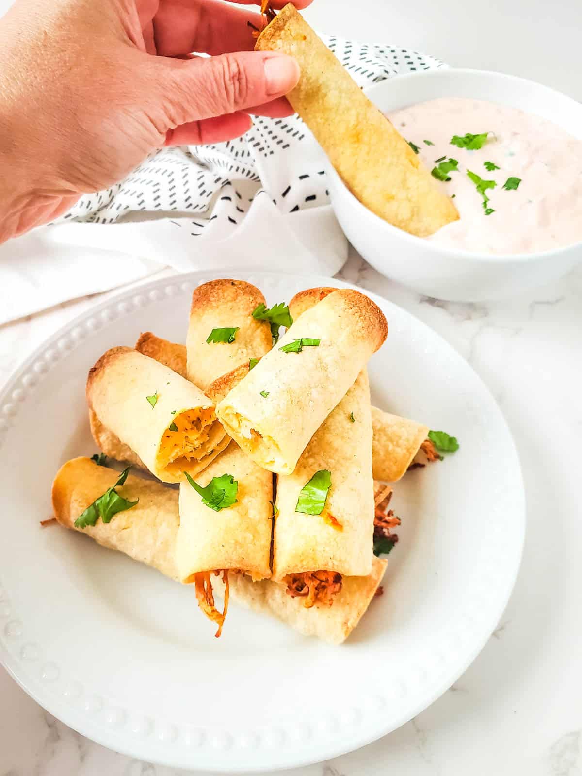 Homemade air fryer chicken taquitos being dipped in sauce.