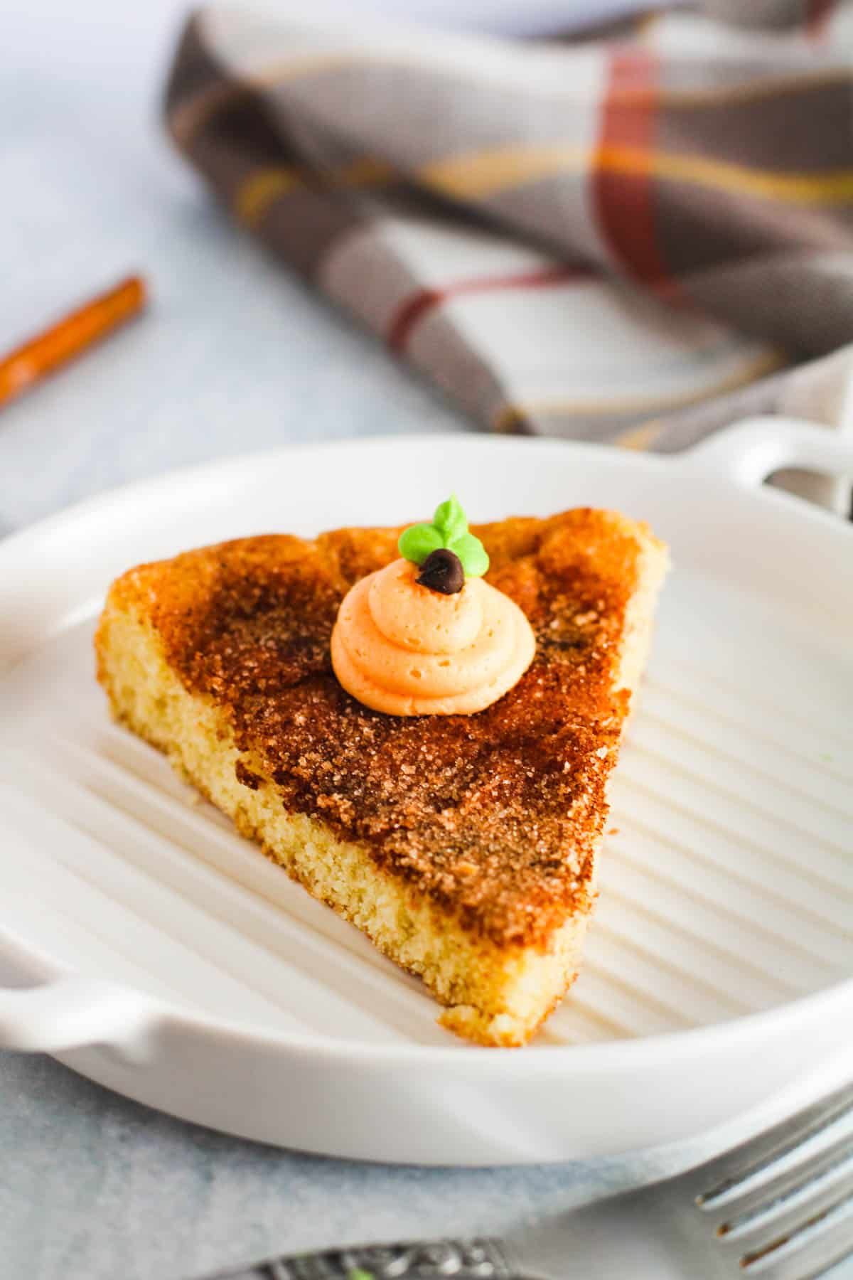 A slice of cookie cake topped with cinnamon and sugar and a frosting pumpkin.