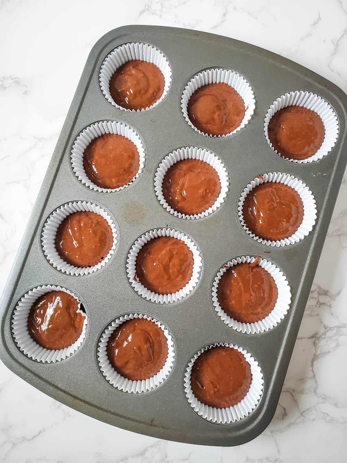 Cupcake tins filled up with snickers cupcake batter.