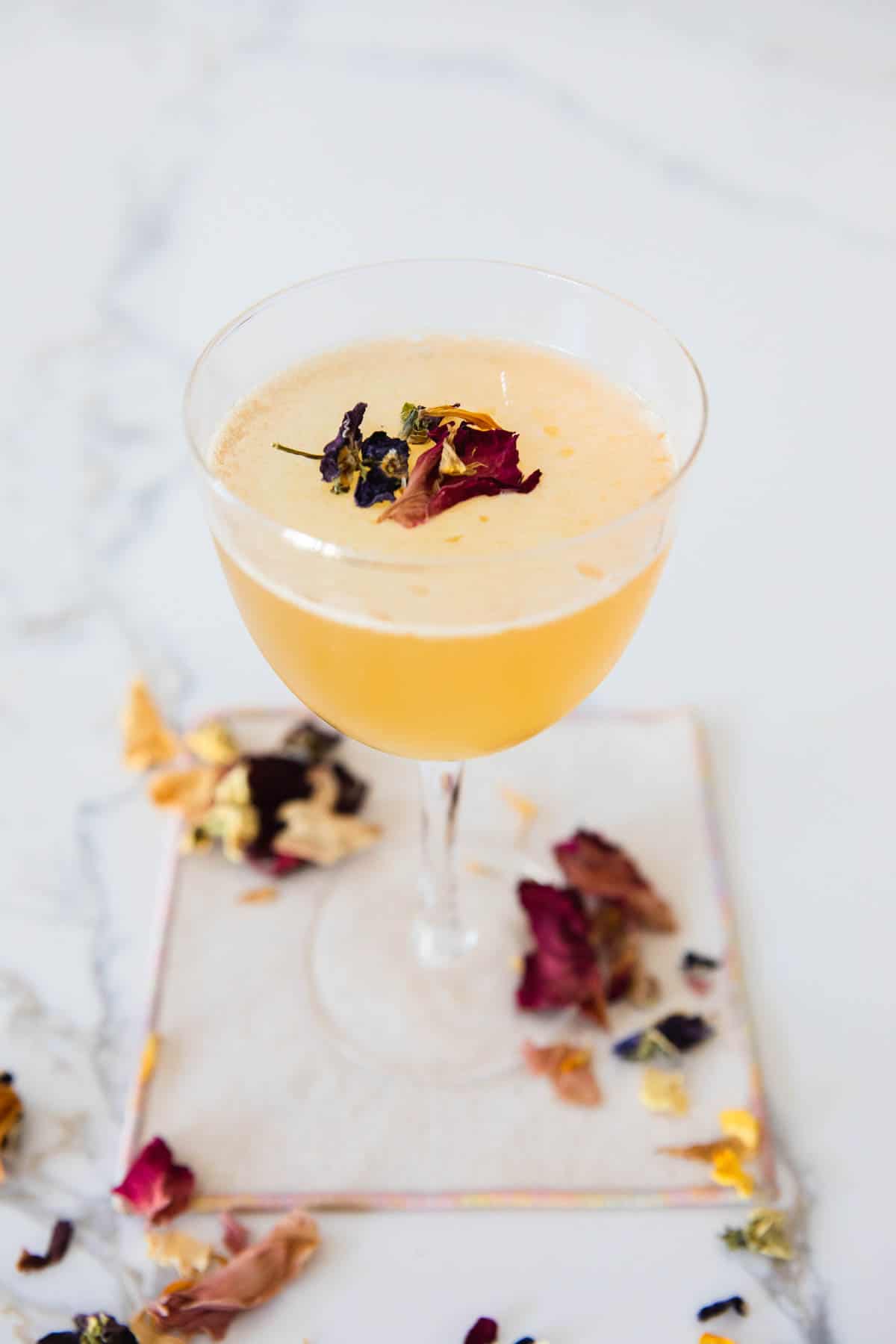 Cocktail glass with an orange cocktail garnished with dried edible flower petals.