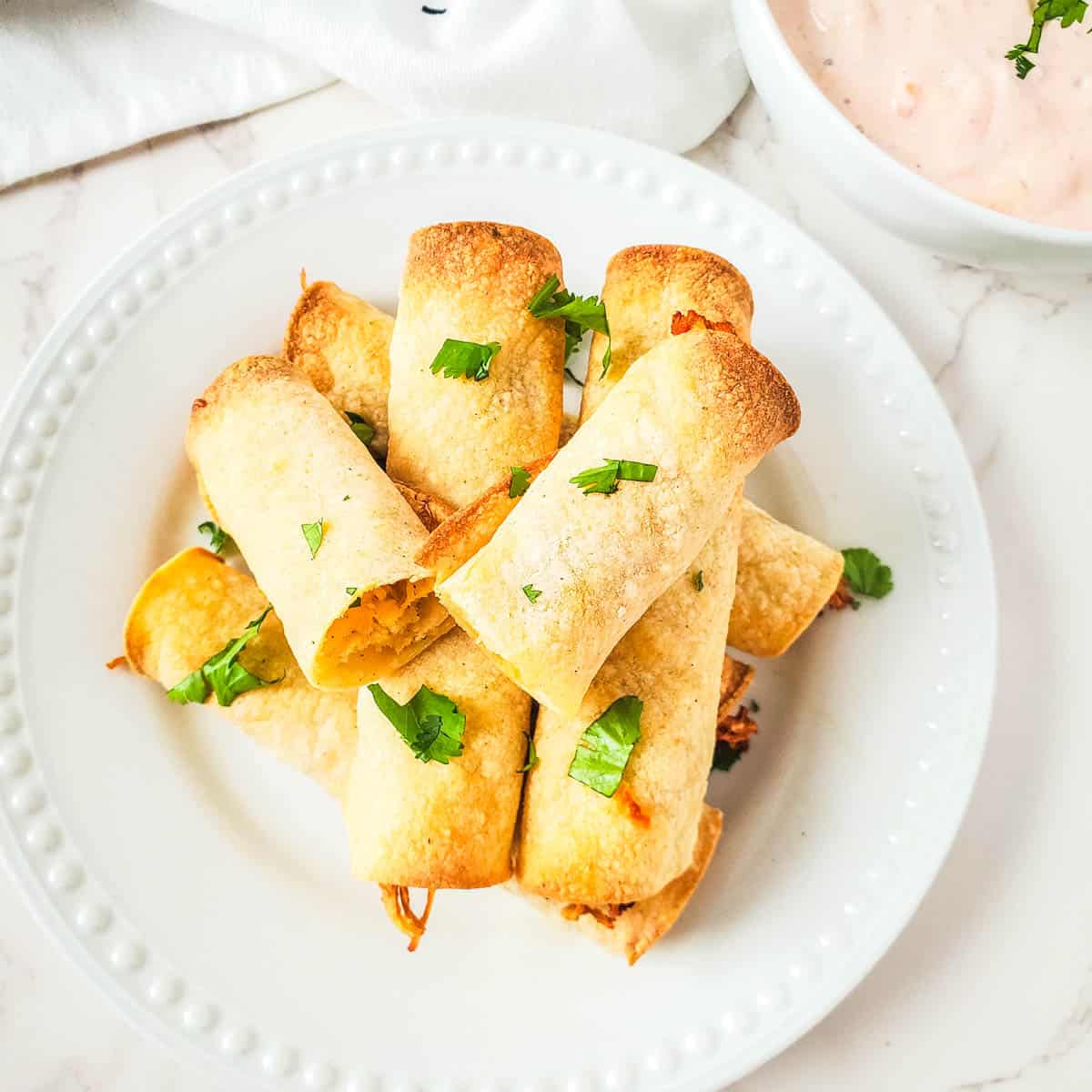 Chicken taquitos with corn tortillas cooked in an air fryer on a white plate. 