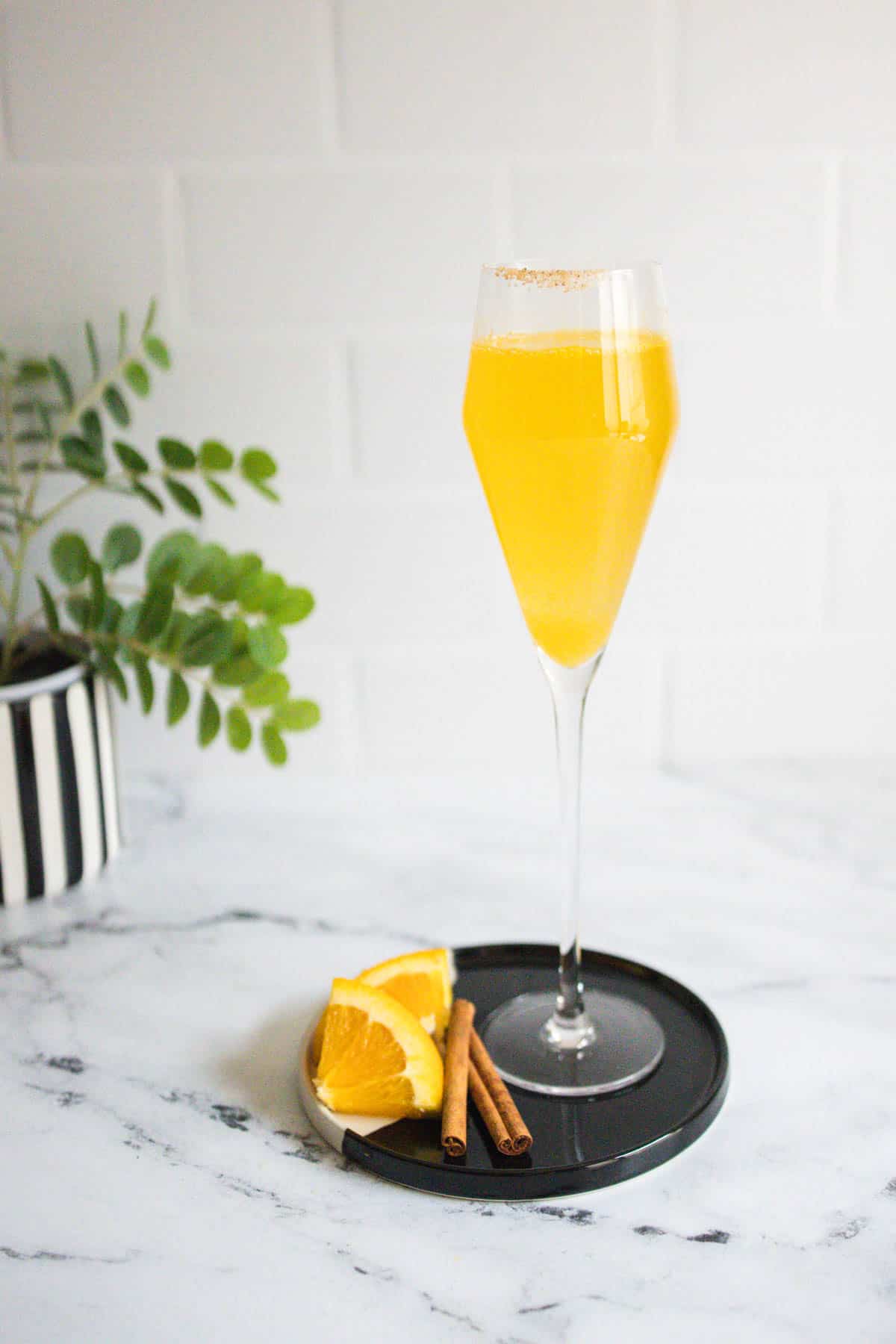 Mimosa with a cinnamon sugar rim on a black cocktail tray.