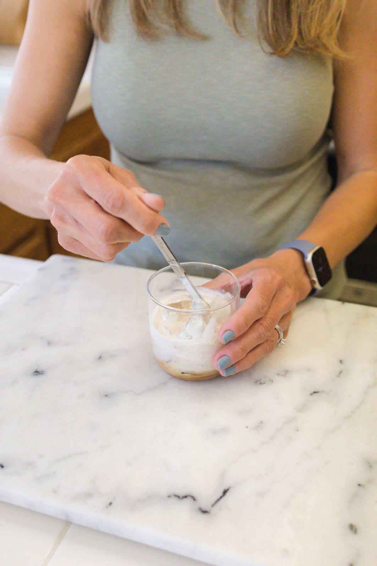 Woman stirring cream into Kahlua and ice.