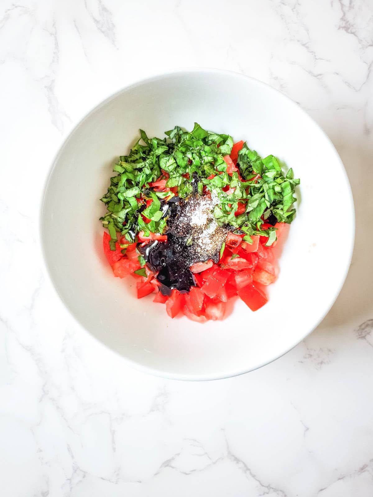 A bowl with chopped tomatoes, basil and seasonings to make a topping for a boursin dip.